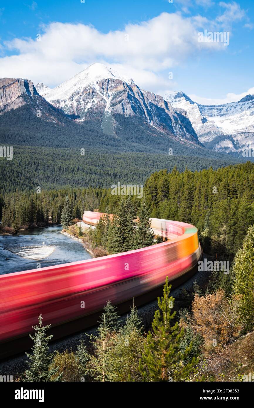 A colorful freight train passes through Morant's Curve in Banff National Park on a sunny Fall morning Stock Photo