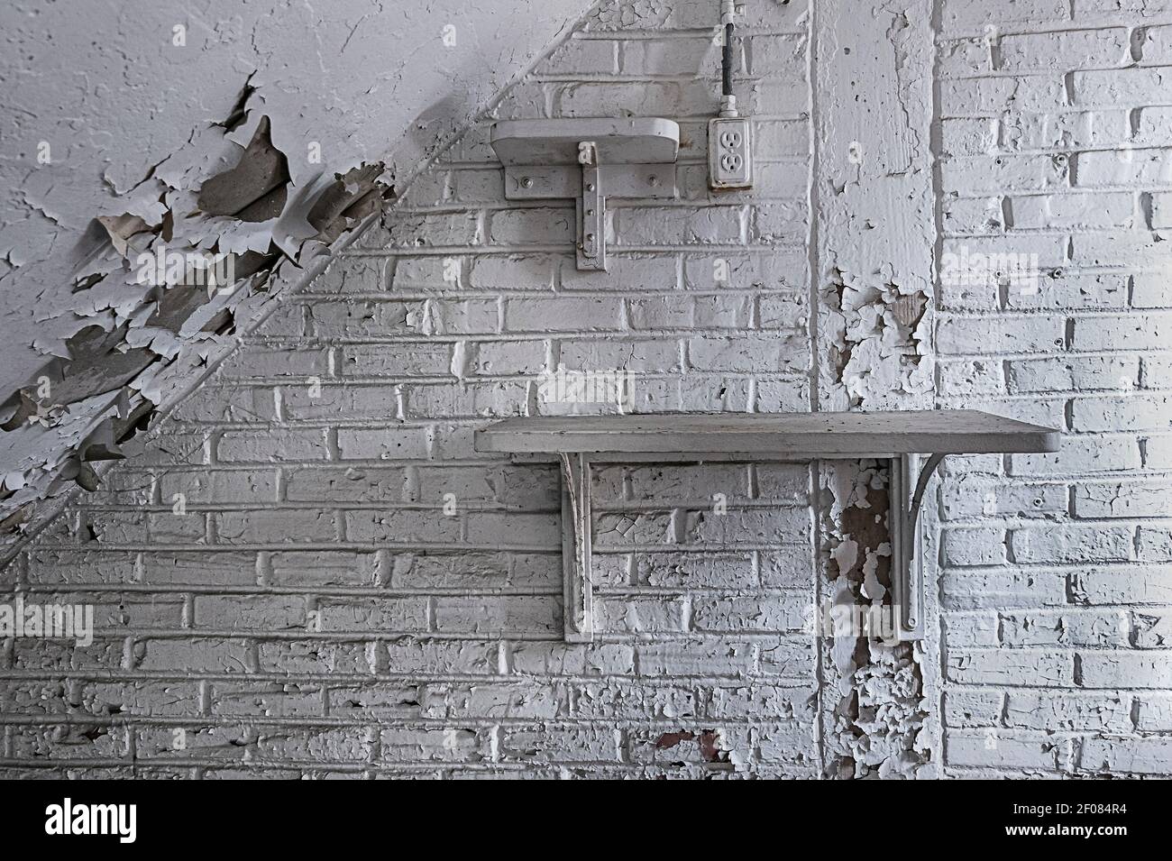 Peeling white paint on brick wall with shelf, interior of dilapidated old building, Philadelphia Pennsylvania USA Stock Photo