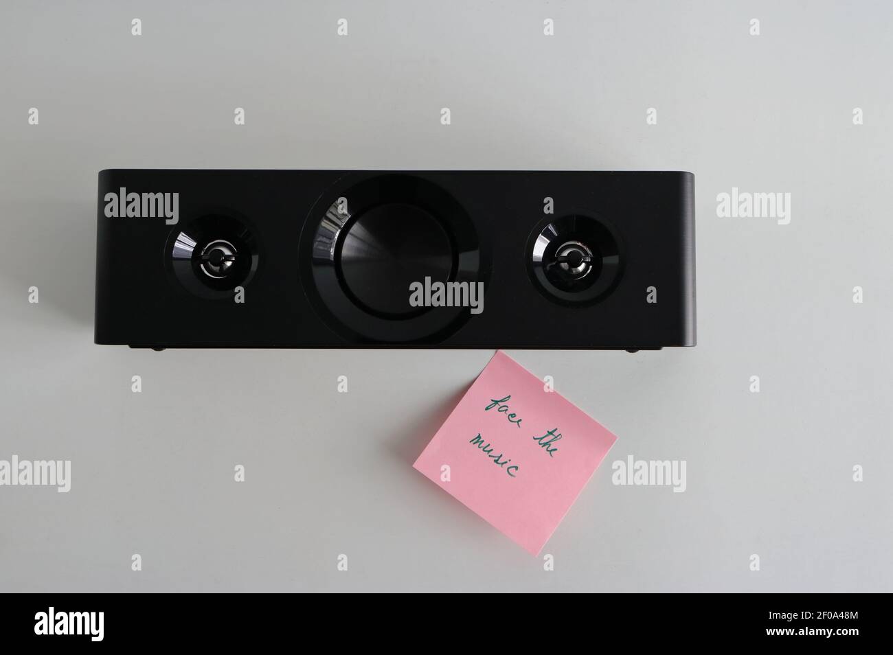 Closeup loudspeaker placed on white wooden table next to sticky note with message face the music, high angle view Stock Photo