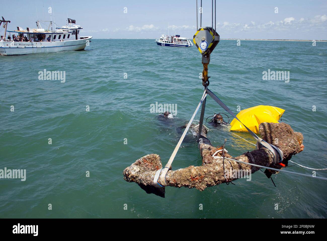 Divers maneuver a 3,000 pound anchor, recovered from the shipwreck of