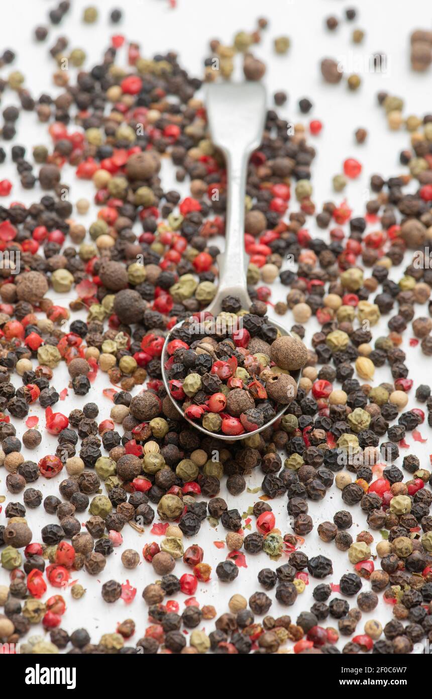 Mixed peppercorns and spoon on a white background Stock Photo