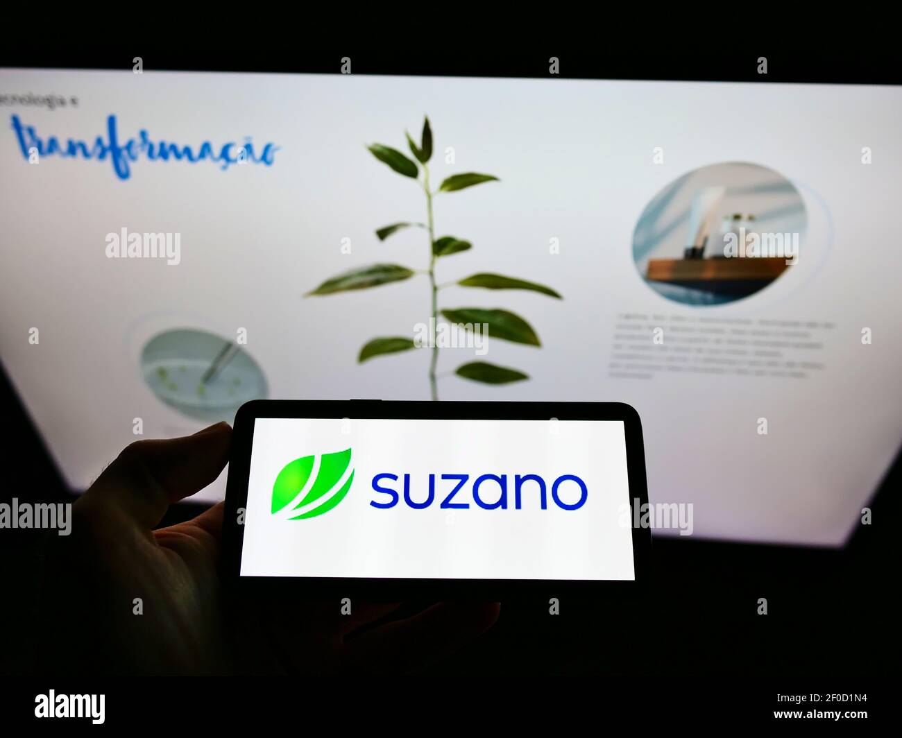 Person holding mobile phone with logo of Brazilian pulp and paper manufacturer Suzano S.A. on screen in front of website. Focus on cellphone display. Stock Photo