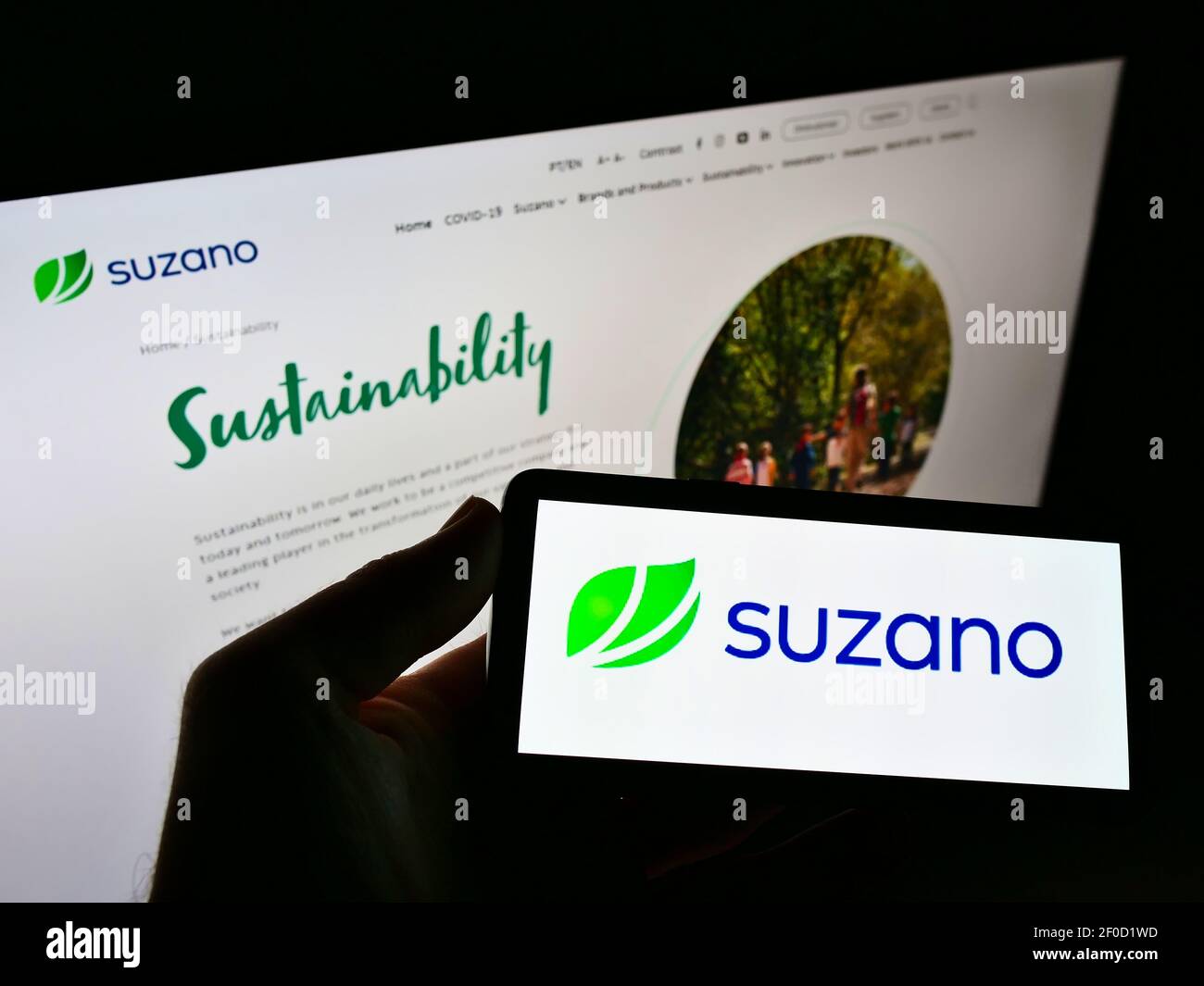 Person holding cellphone with logo of Brazilian pulp and paper producer Suzano S.A. on screen in front of company web page. Focus on phone display. Stock Photo