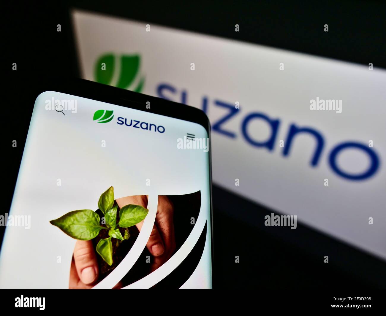 Smartphone with website of Brazilian pulp and paper manufacturer Suzano S.A. on screen in front of company logo. Focus on center of phone display. Stock Photo