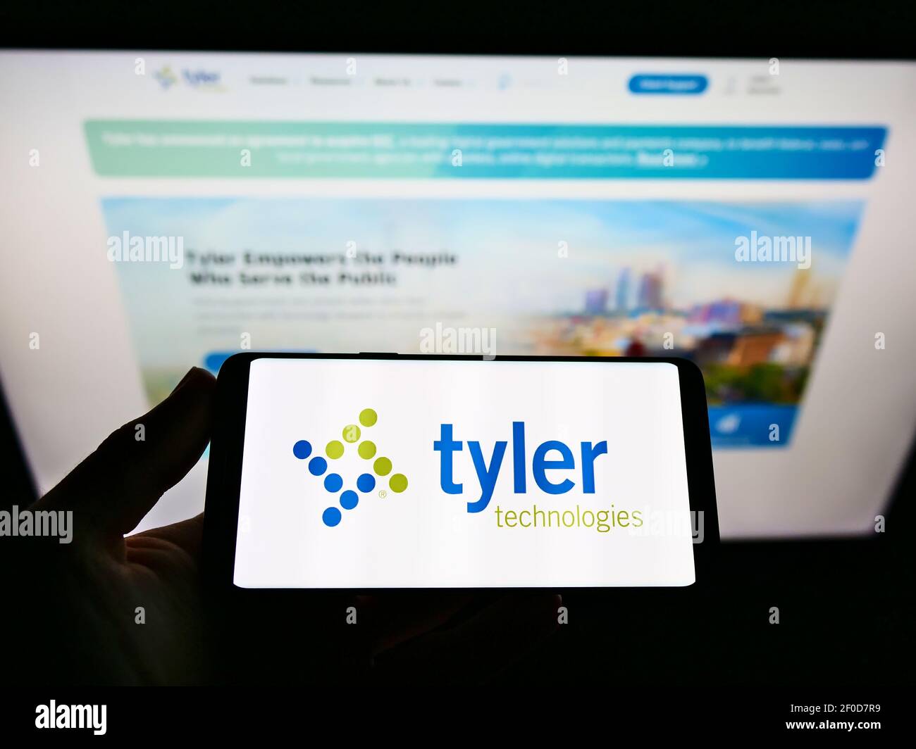 person-holding-mobile-phone-with-business-logo-of-us-software-company-tyler-technologies-inc-on-screen-in-front-of-web-page-focus-on-phone-display-stock-photo-alamy