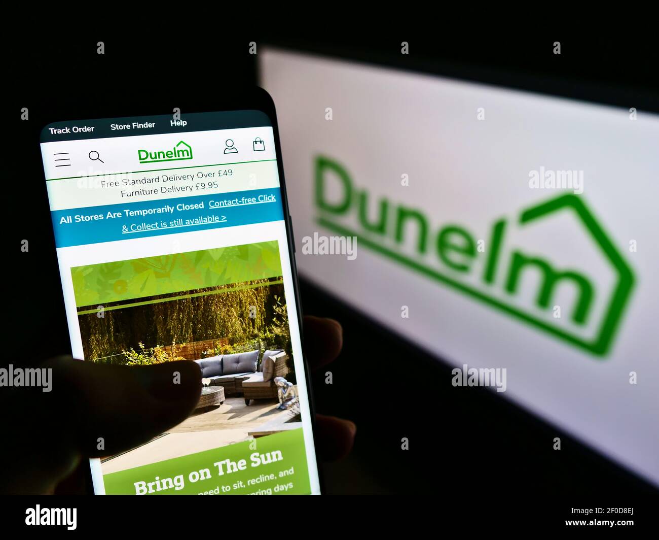 Person holding cellphone with website of British furnishing retailer Dunelm Group on screen in front of logo. Focus on center of phone display. Stock Photo