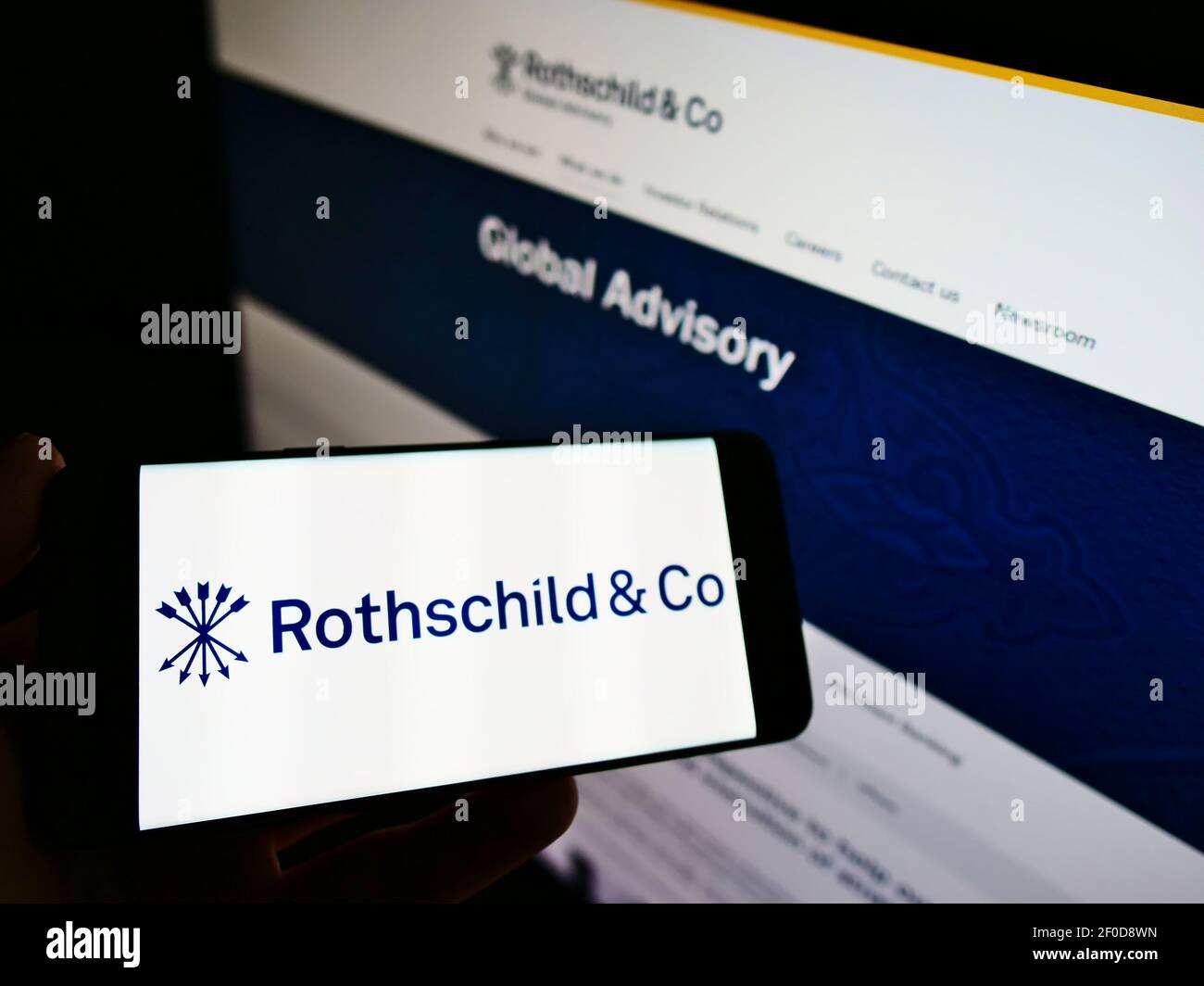 Person holding cellphone with logo of French financial services company Rothschild and Co. SCA on screen in front of webpage. Focus on phone display. Stock Photo