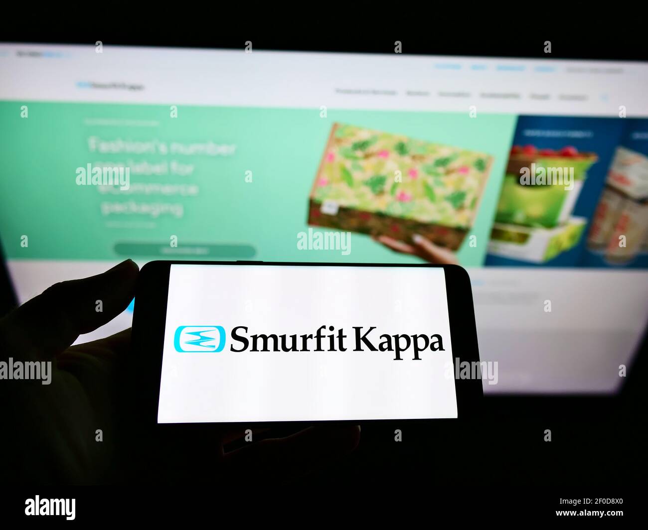 Person holding cellphone with business logo of Irish packaging company Smurfit Kappa Group plc on screen in front of webpage. Focus on phone display. Stock Photo