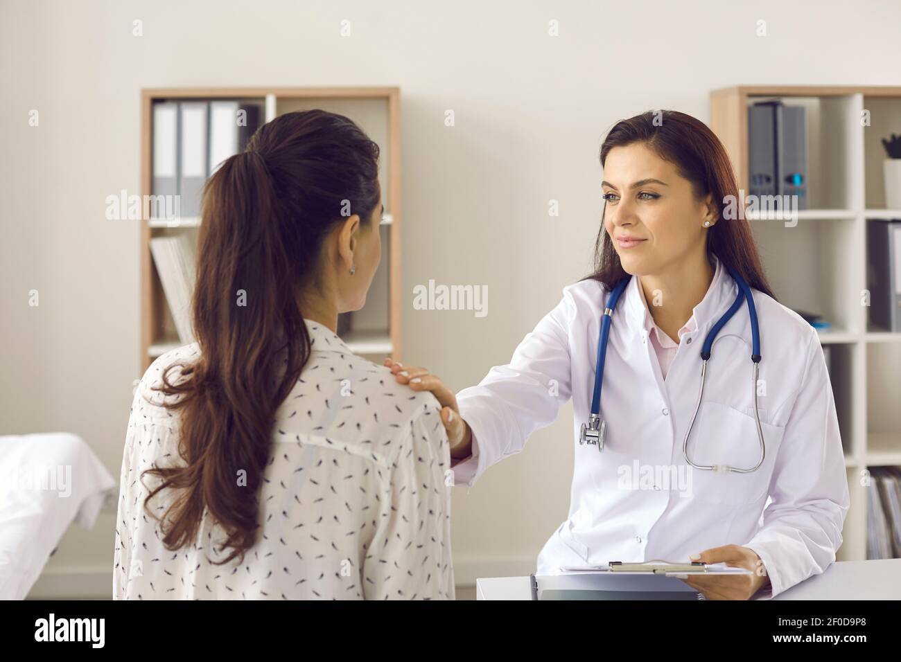 Doctor talking to young woman and touching her shoulder to reassure, support and cheer up Stock Photo