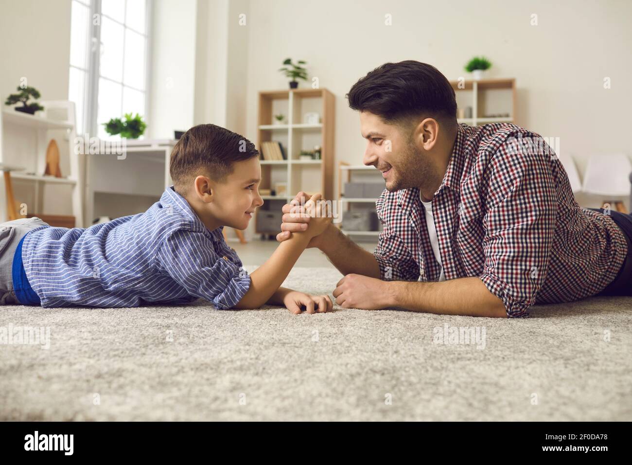 Young father and his cute little son competing in arm wrestling while lying on floor. Stock Photo