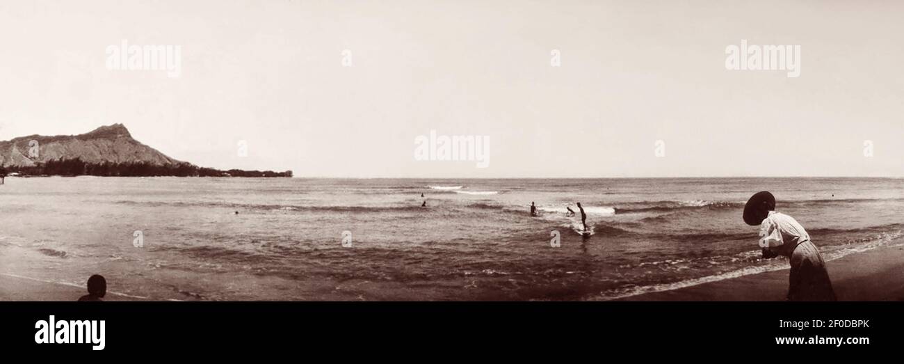 Panoramic beachscape view of surfer riding a wave at Waikiki Beach, Honolulu, Territory of Hawaii in 1907. Stock Photo