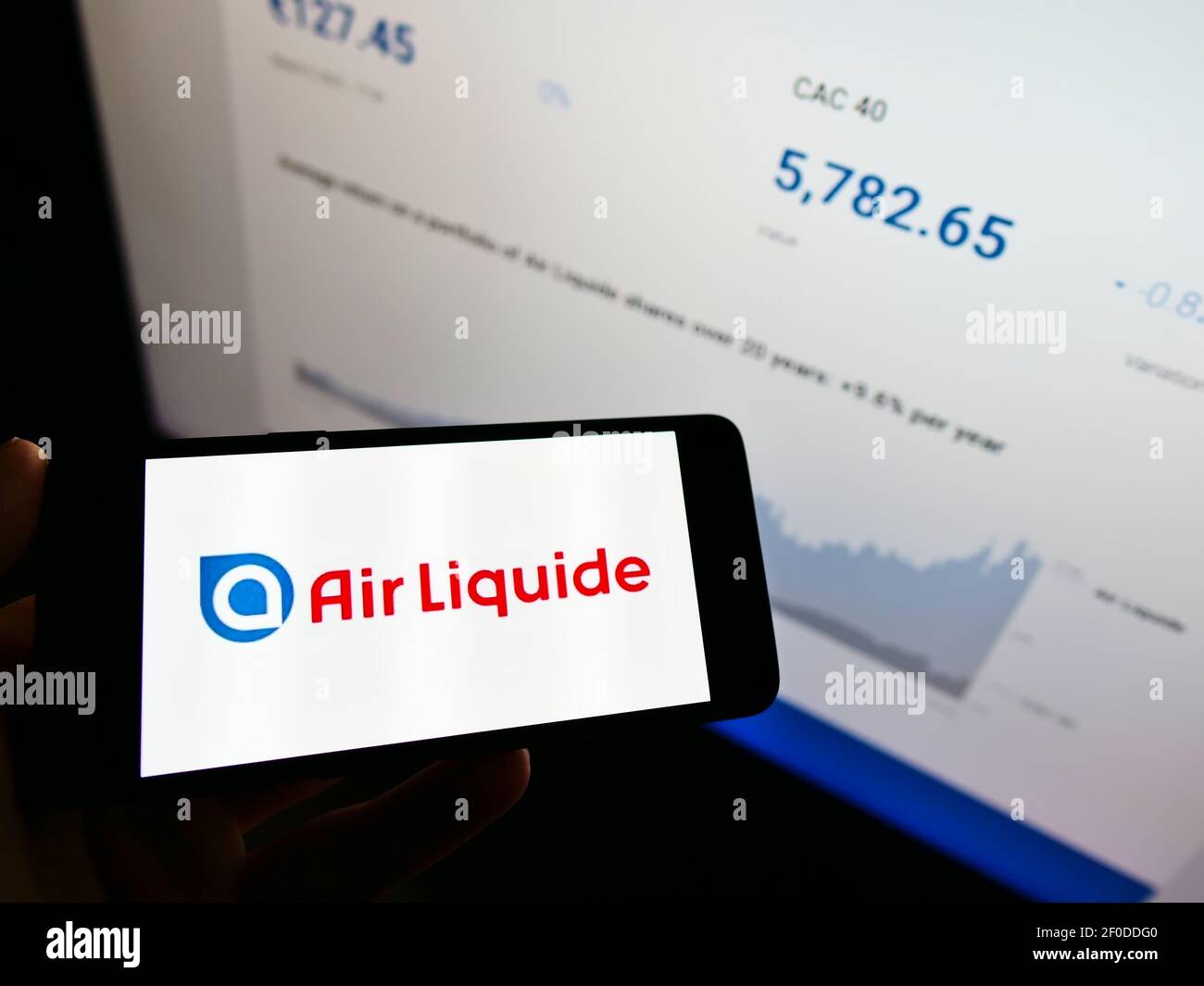 Person holding cellphone with logo of French chemical company Air Liquide SA on screen in front of website with stock chart. Focus on phone display. Stock Photo