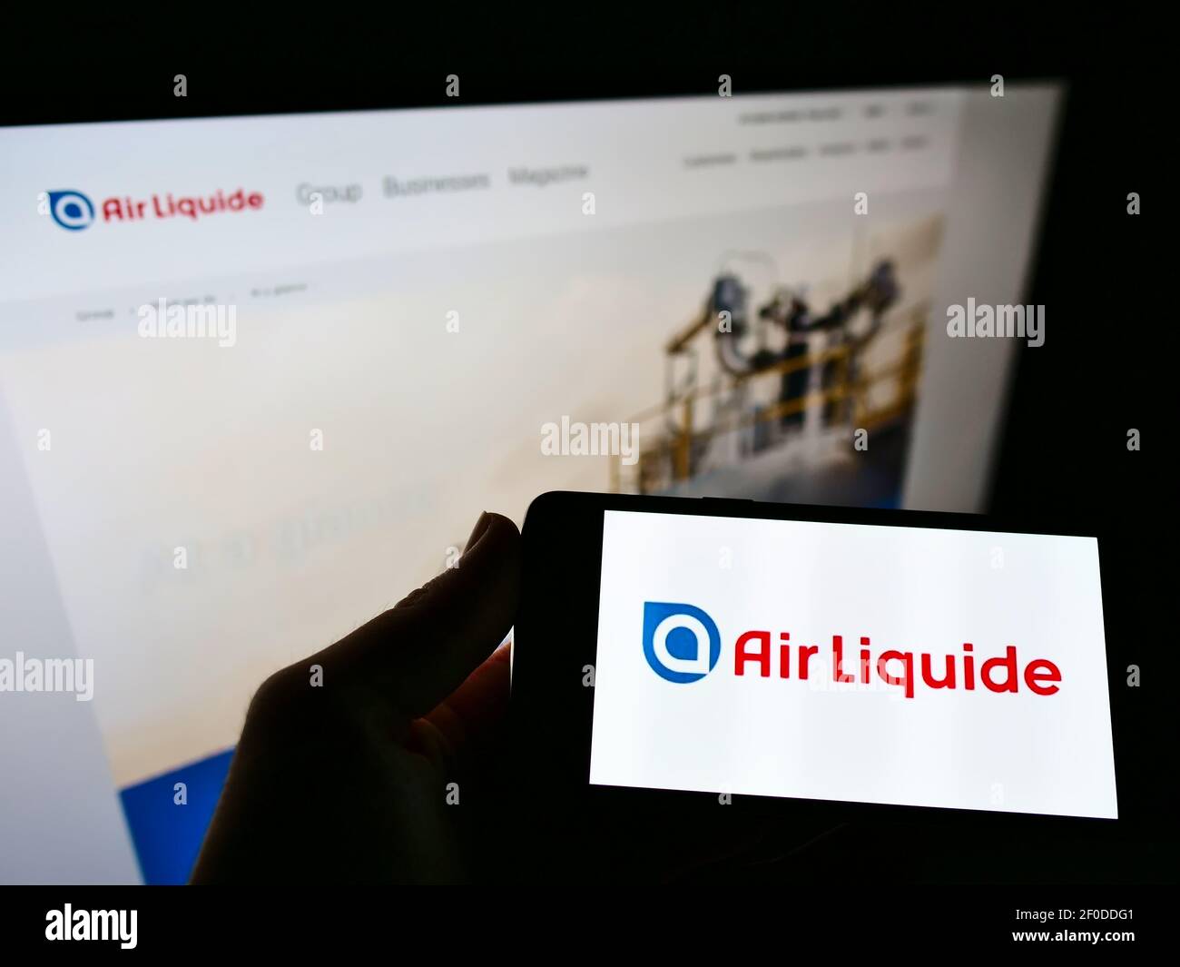 Person holding smartphone with logo of French chemical company Air Liquide S.A. on screen in front of website. Focus on phone display. Stock Photo