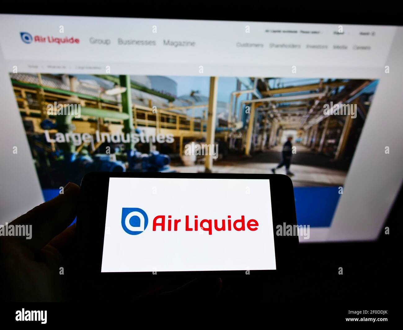 Person holding mobile phone with business logo of French chemical company Air Liquide SA on screen in front of webpage. Focus on cellphone display. Stock Photo