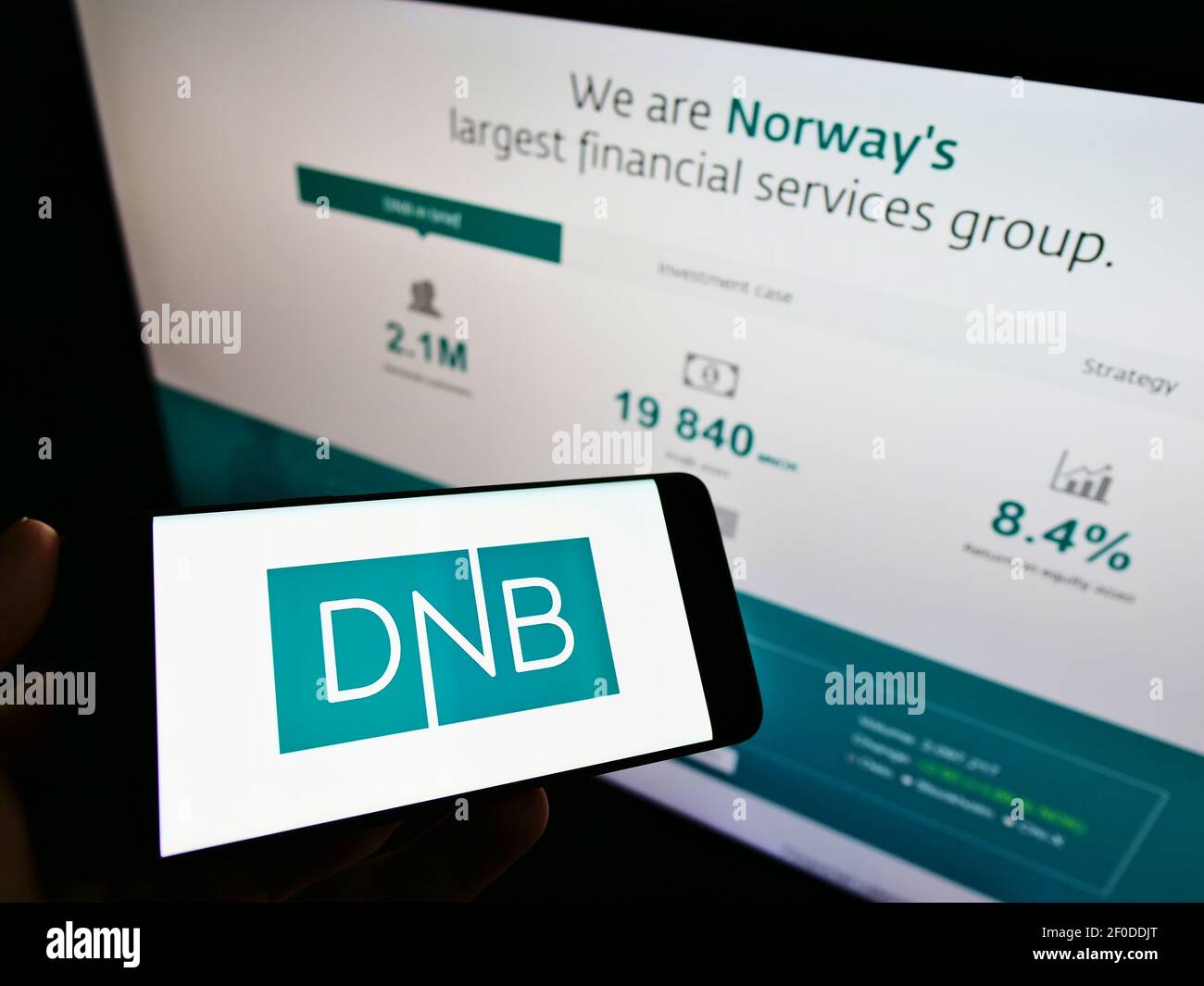 Person holding cellphone with business logo of Norwegian financial services company DNB ASA on screen in front of web page. Focus on phone display. Stock Photo