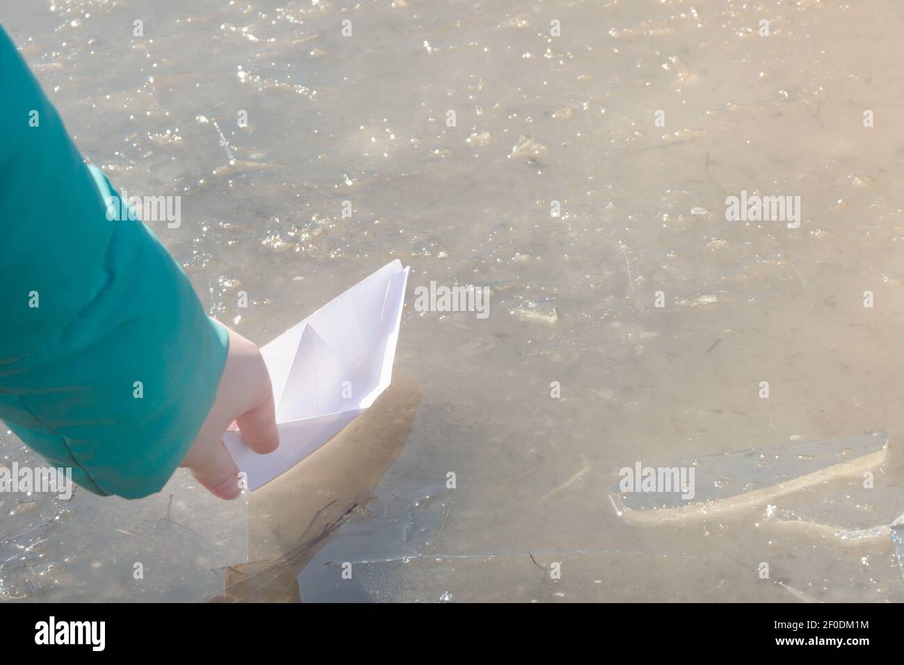 White paper ship is sent on journey into first spring puddle. Child's hand with origami in sunlight. Early spring mood concept, freedom. Stock Photo