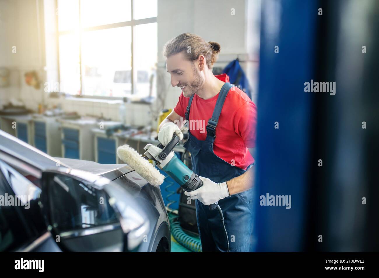 Smiling repairman grinding car body in garage Stock Photo