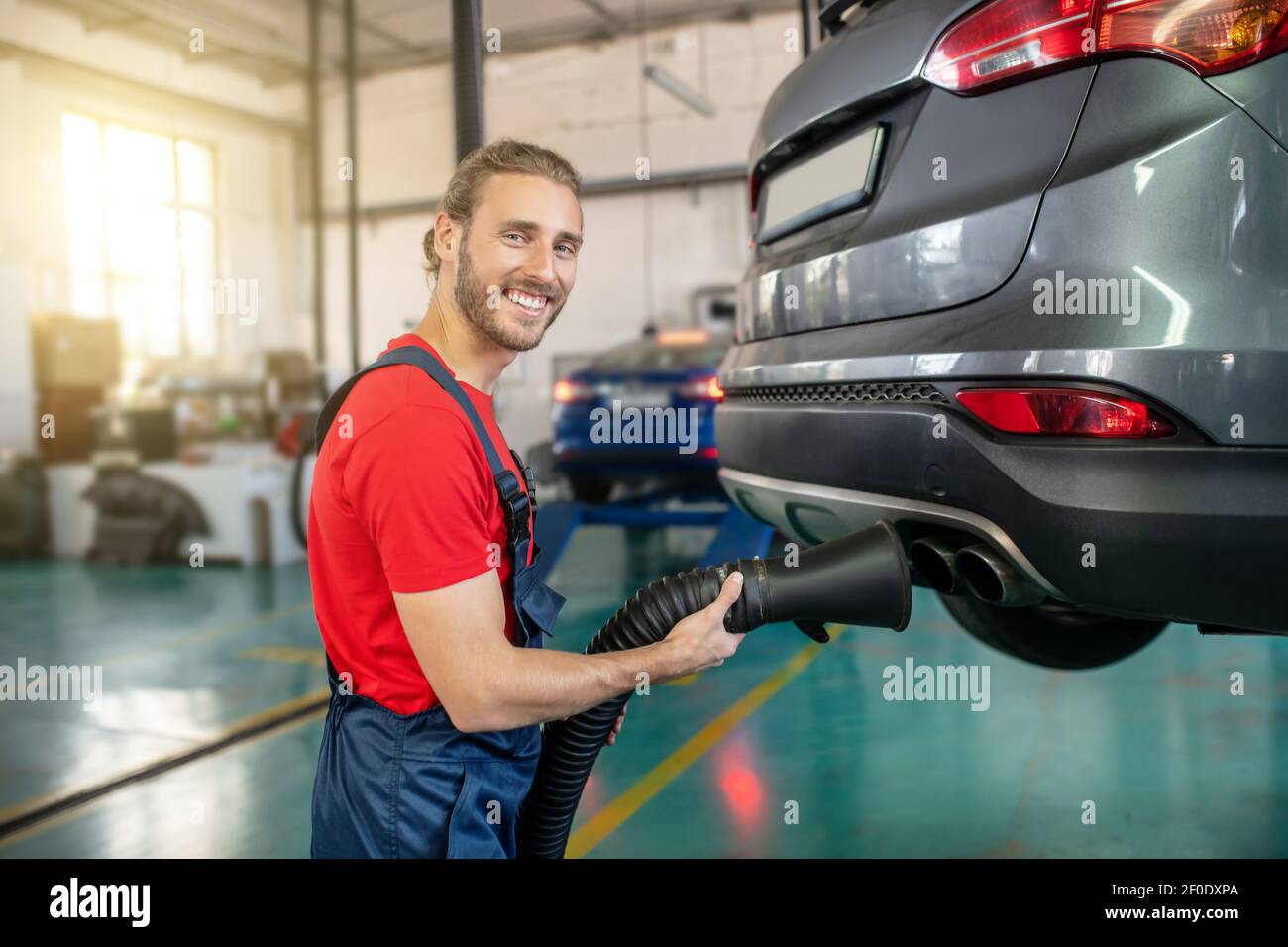 Smiling man with hose near exhaust pipe of auto Stock Photo