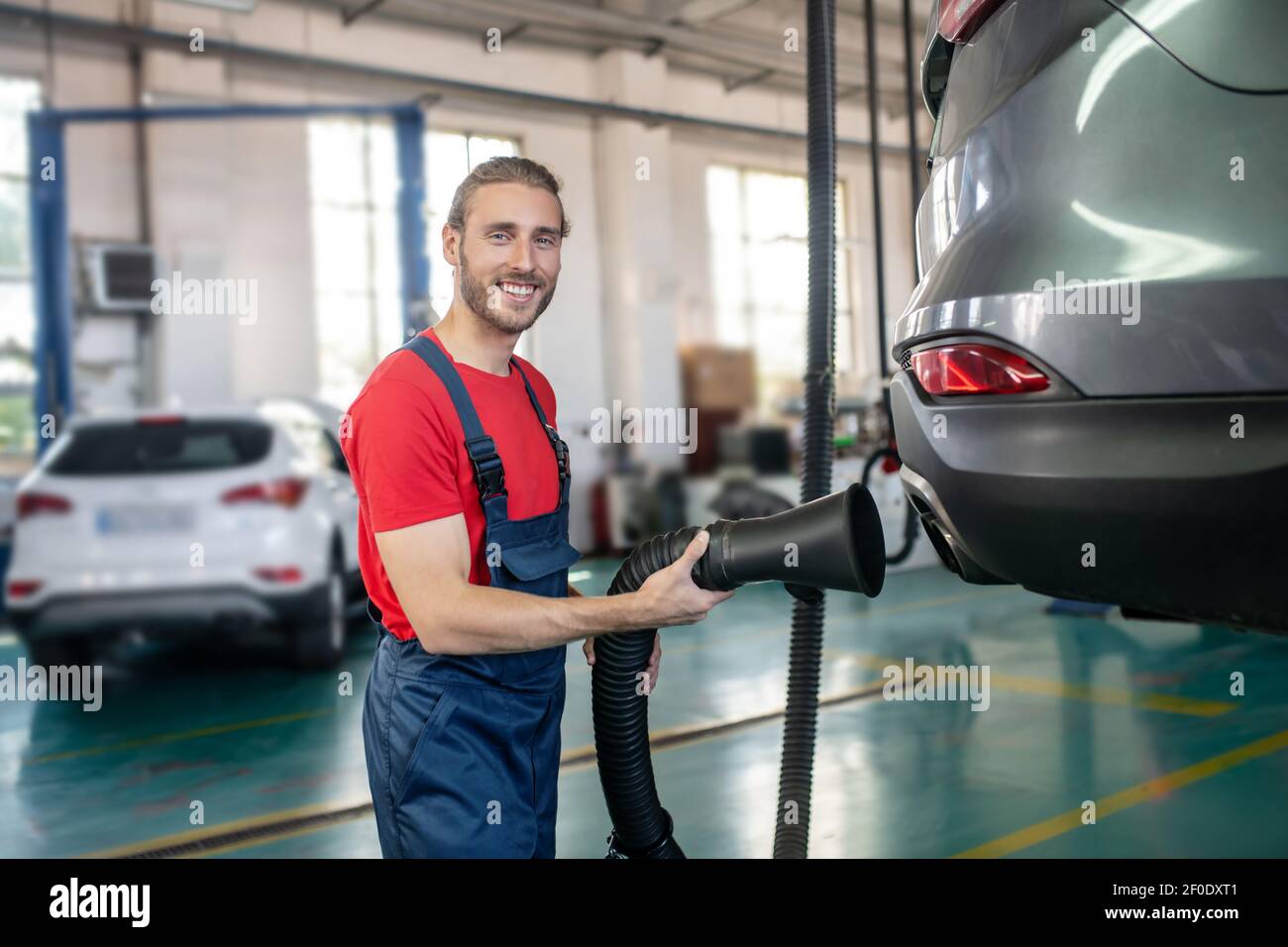 Car repairer with hose near car in garage Stock Photo