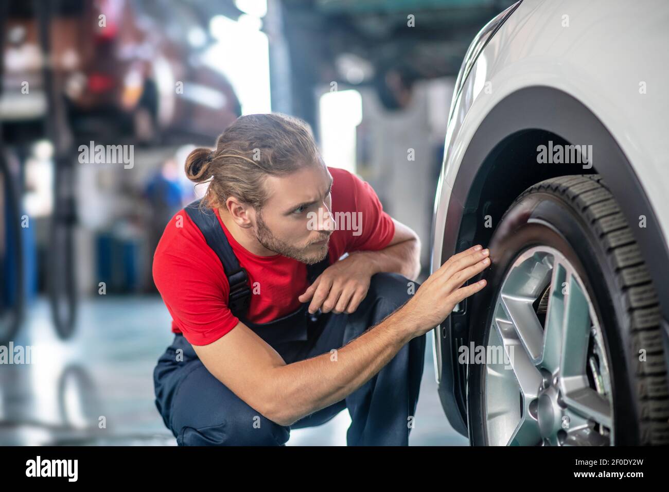 Repairman examining car wheel in garage Stock Photo