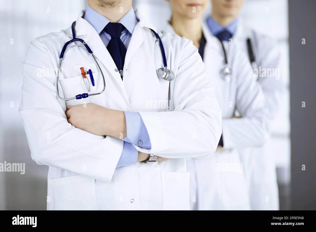 Group of modern doctors standing as a team with crossed arms and stethoscopes in hospital office. Physicians ready to examine and help patients Stock Photo