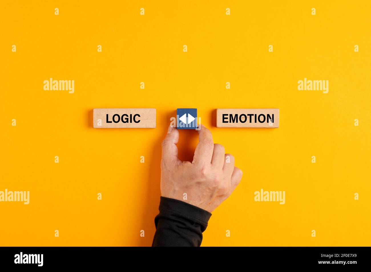 Male hand holds a wooden cube with arrow icon between the options of logic or emotion. Emotional or logical decision making concept. Stock Photo