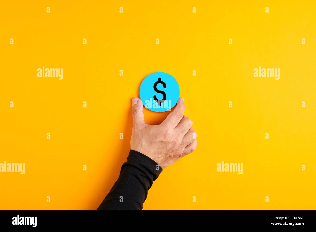 Male hand placing a blue badge with a US dollar currency sign on yellow background. Stock Photo