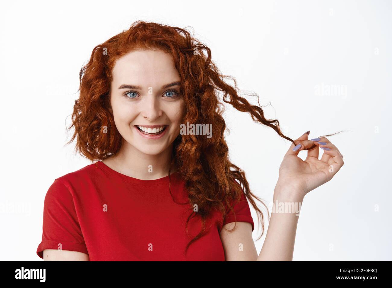 Portrait of confident beautiful ginger girl with curly hairstyle, playing with curl strand and