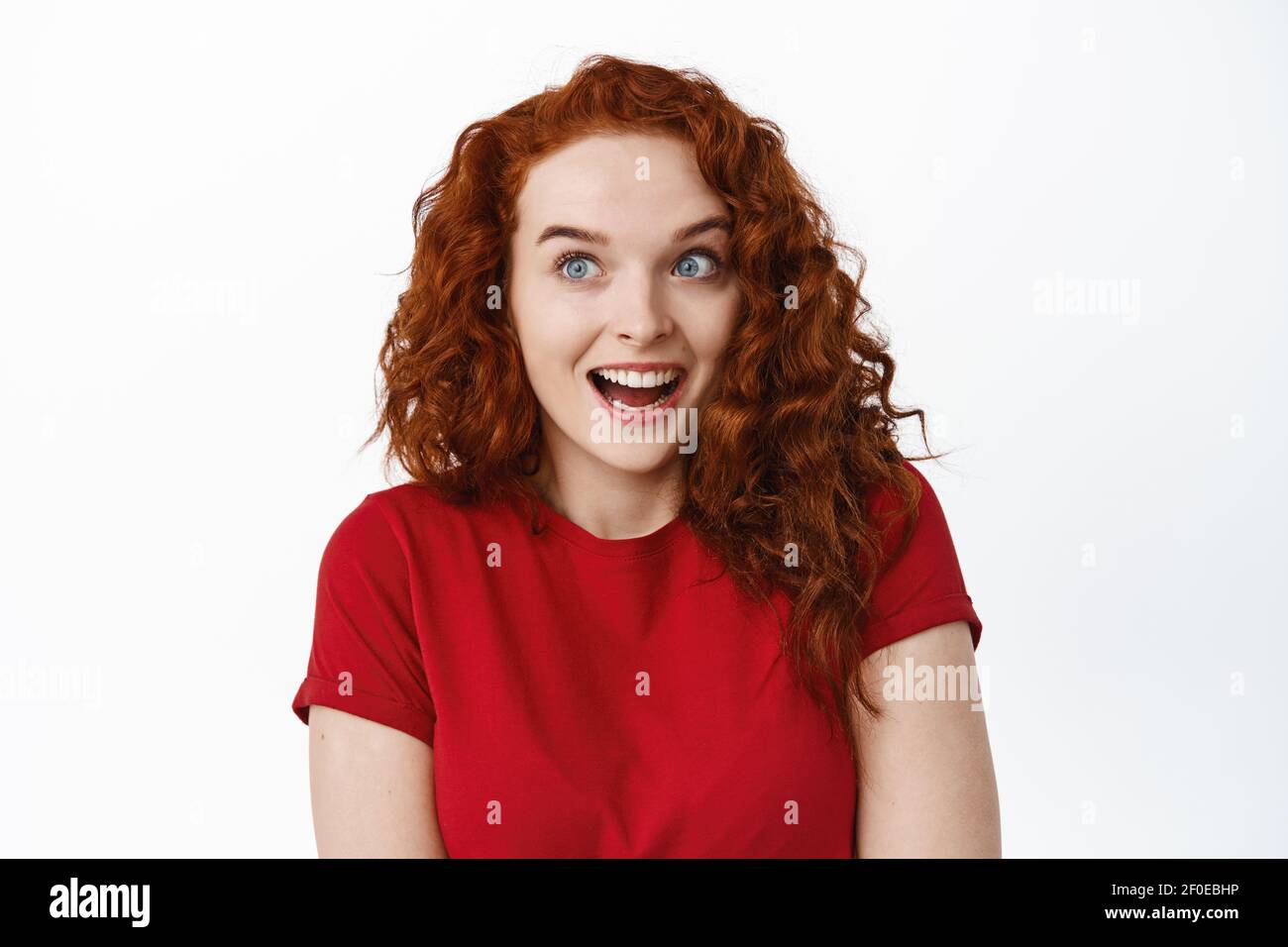 Close-up of surprised candid girl with natural red hair and pale skin, open mouth excited, staring left with dropped jaw and amazed face, white Stock Photo