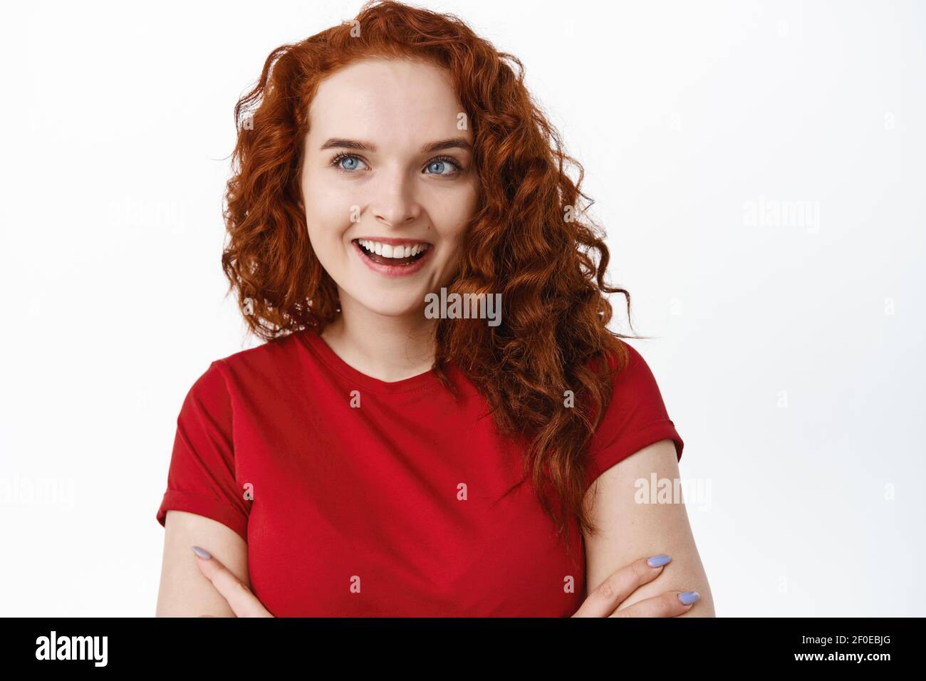 Close-up of silly beautiful girl with ginger curly hair, looking aside at left side logo or advertisement, smiling pleased and determined to buy Stock Photo