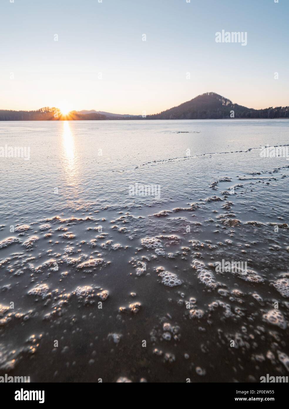 Brightened piece of ice in warm rays of sunset. Frozen shards of broken ice and lots of frozen bubbles. The structure of the ice in the lake Stock Photo