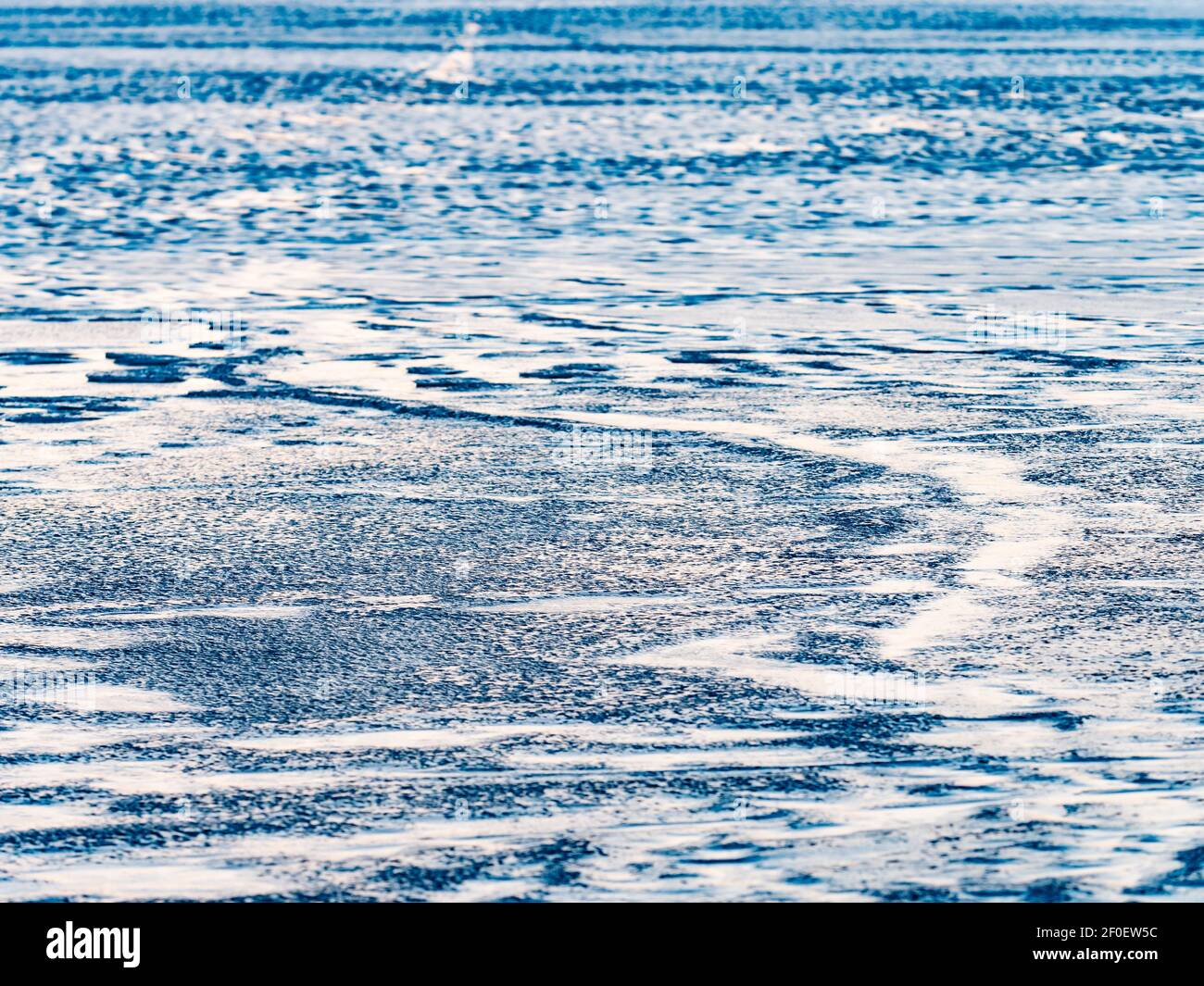 Bubbles and pieces of clear natural ice on frozen lake in evening sun. The melting changet the flat surface of ice to puddle with shards Stock Photo