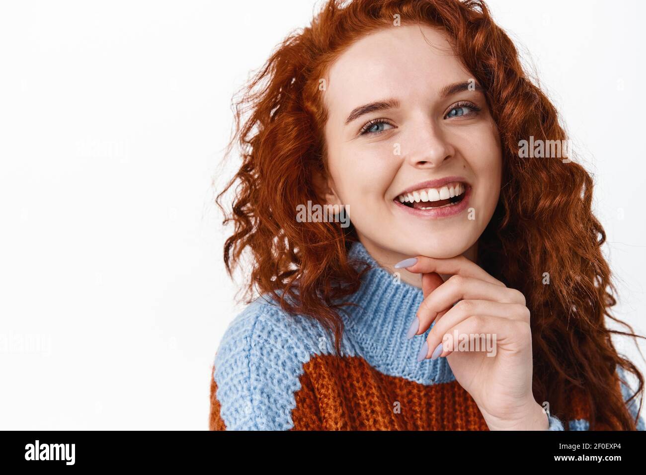 Close up portrait of redhead woman with curly natural healthy hair and pale smooth skin, touching clean and fresh face, smiling and laughing while Stock Photo