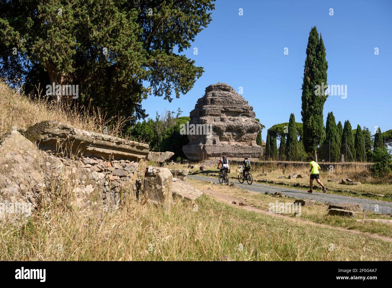Rome. Italy. Via Appia Antica (Appian Way), people walking and riding bikes amongst ancient Roman funerary monuments.  The so-called Pyramid Mausoleum Stock Photo