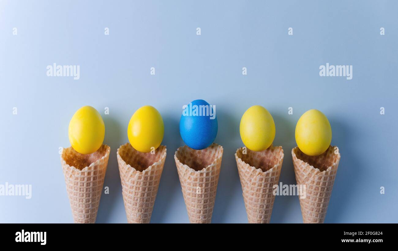 Yellow eggs and one blue in waffle cones lie on a blue horizontal background. Easter background concept flat lay, copy space, selective focus Stock Photo