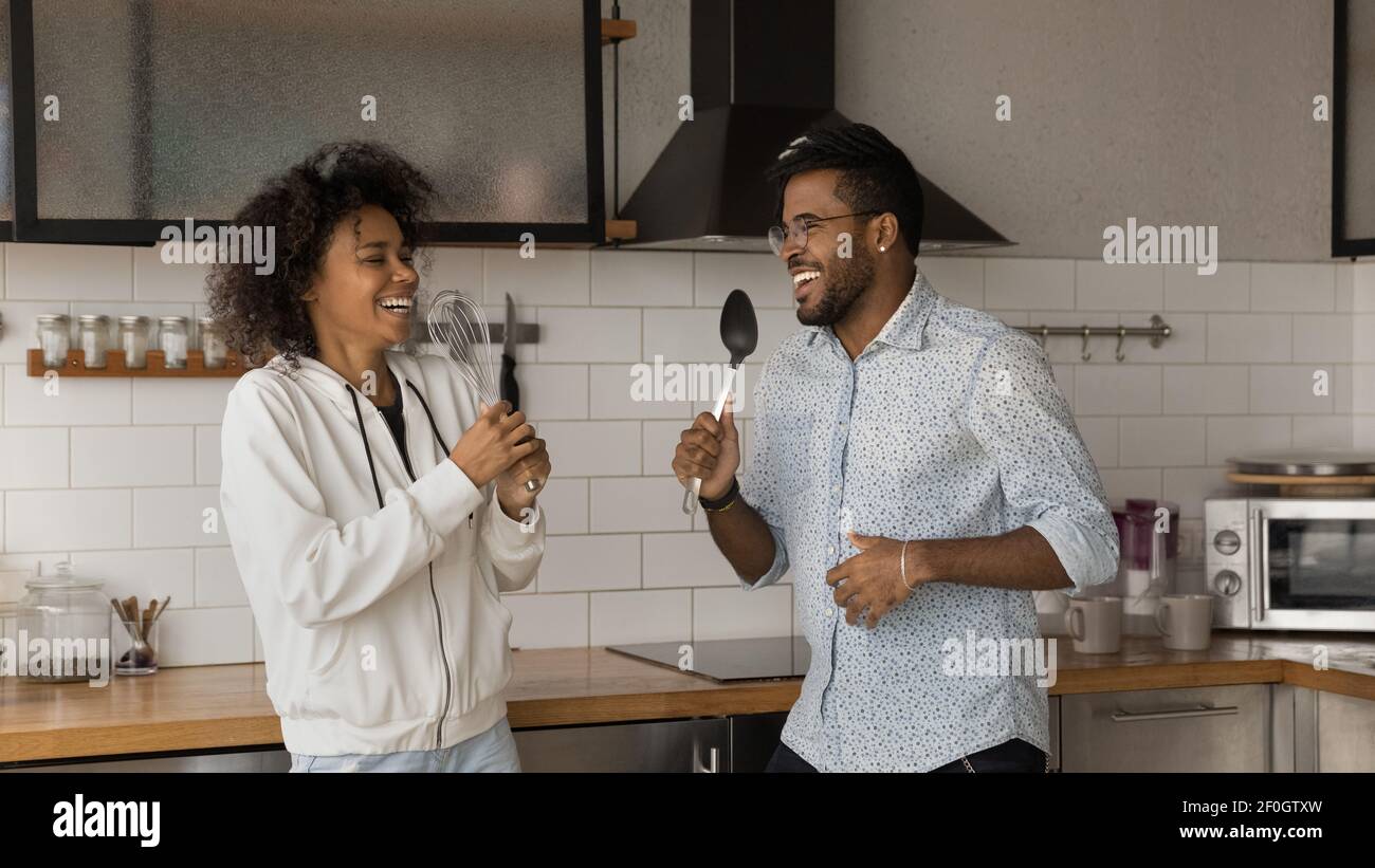 Overjoyed African American couple having fun with kitchenware in kitchen Stock Photo