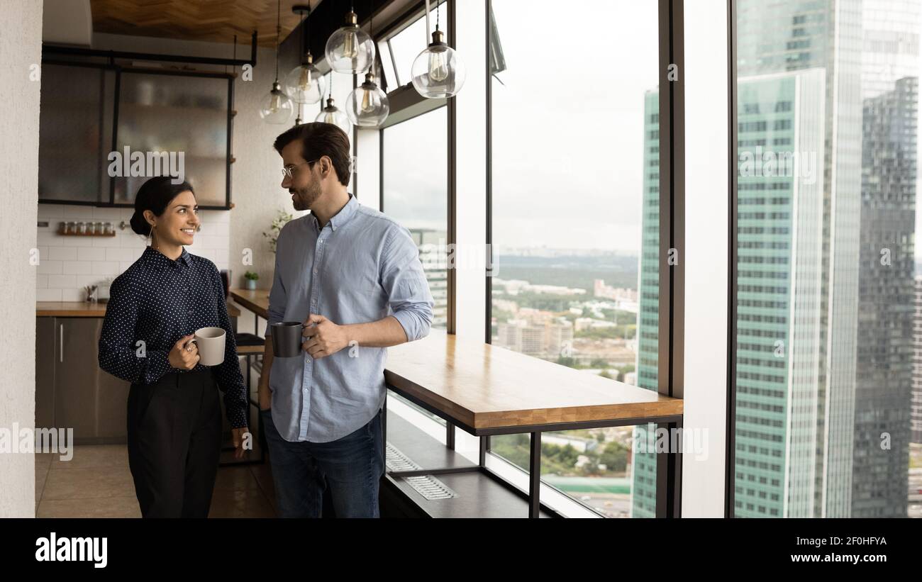 Diverse colleagues chatting, holding cups, standing in kitchen Stock Photo