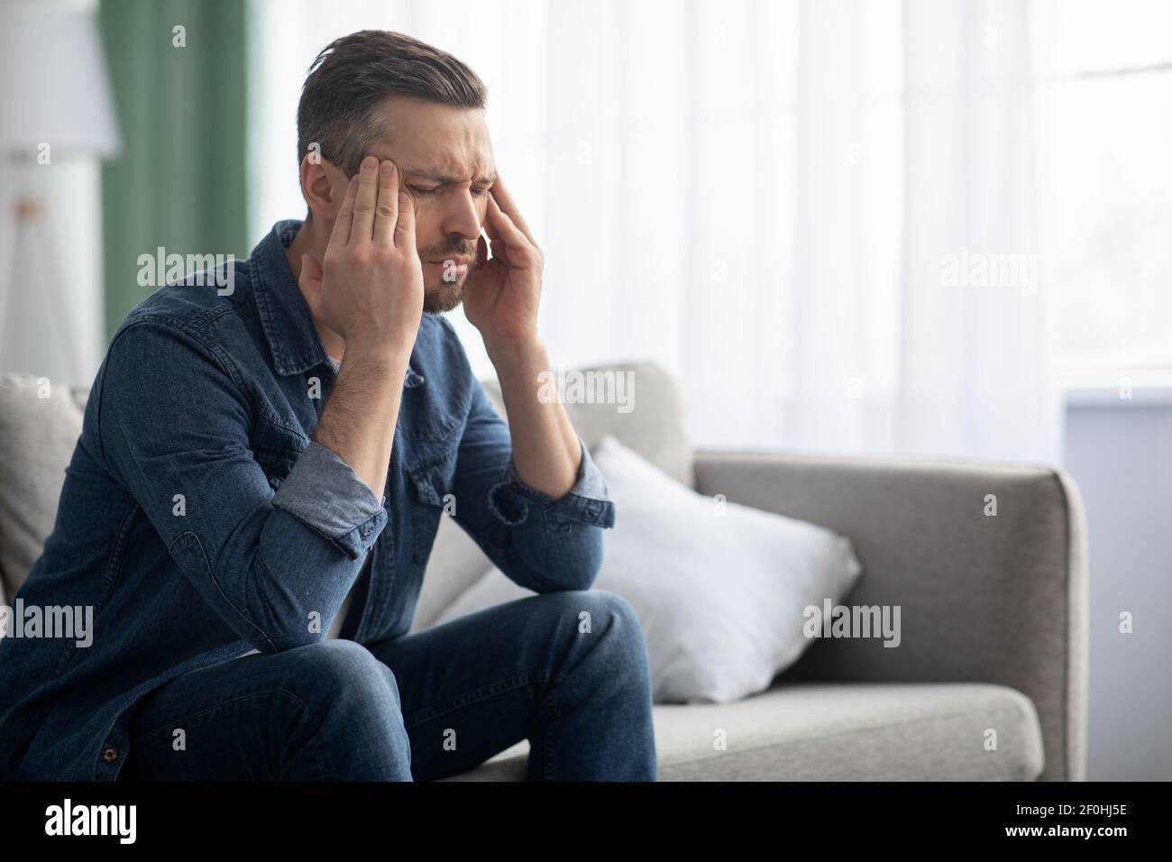 Stressed man having headache, sitting on sofa at home Stock Photo
