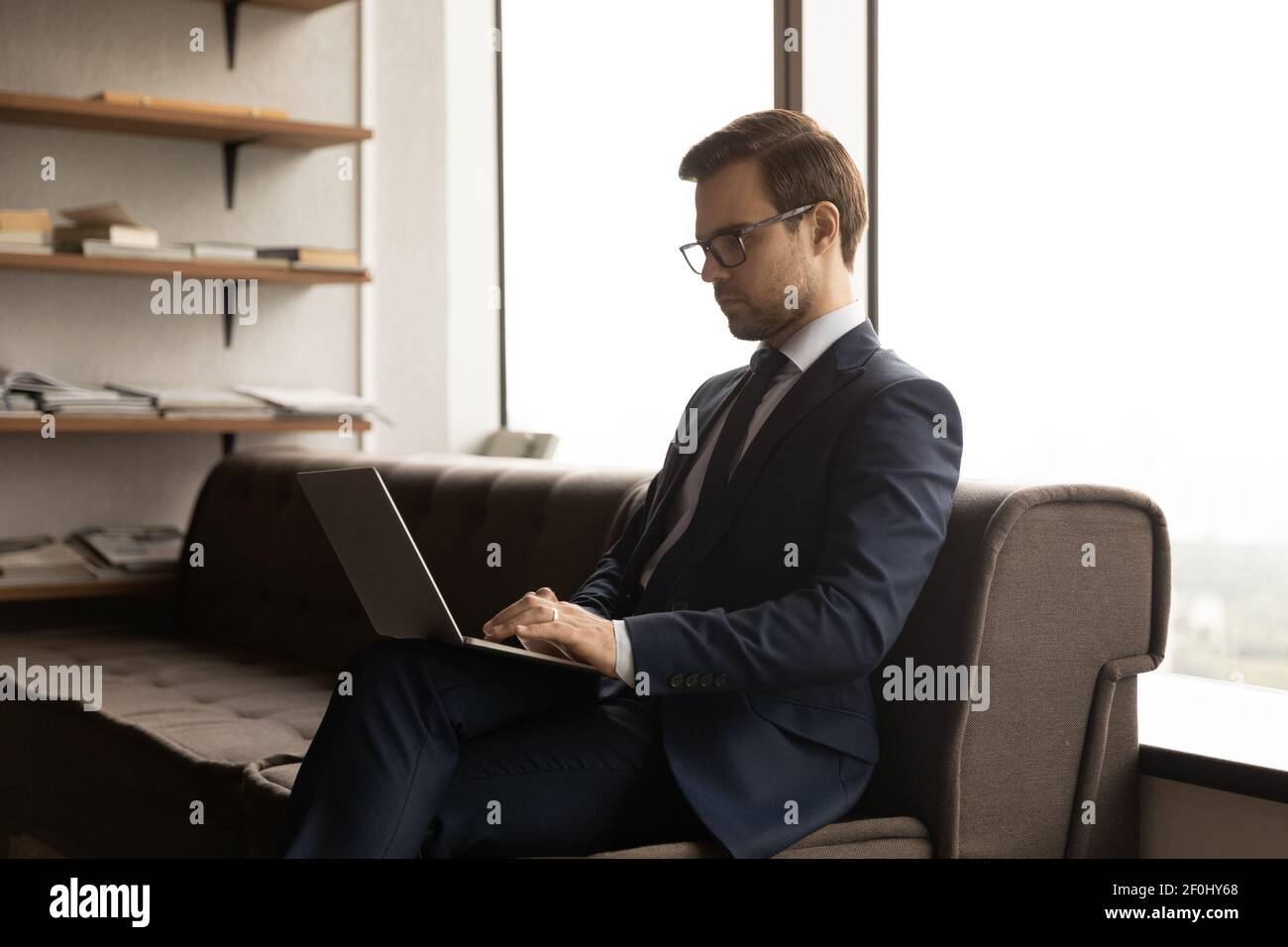 Close up confident businessman wearing glasses and suit using laptop Stock Photo