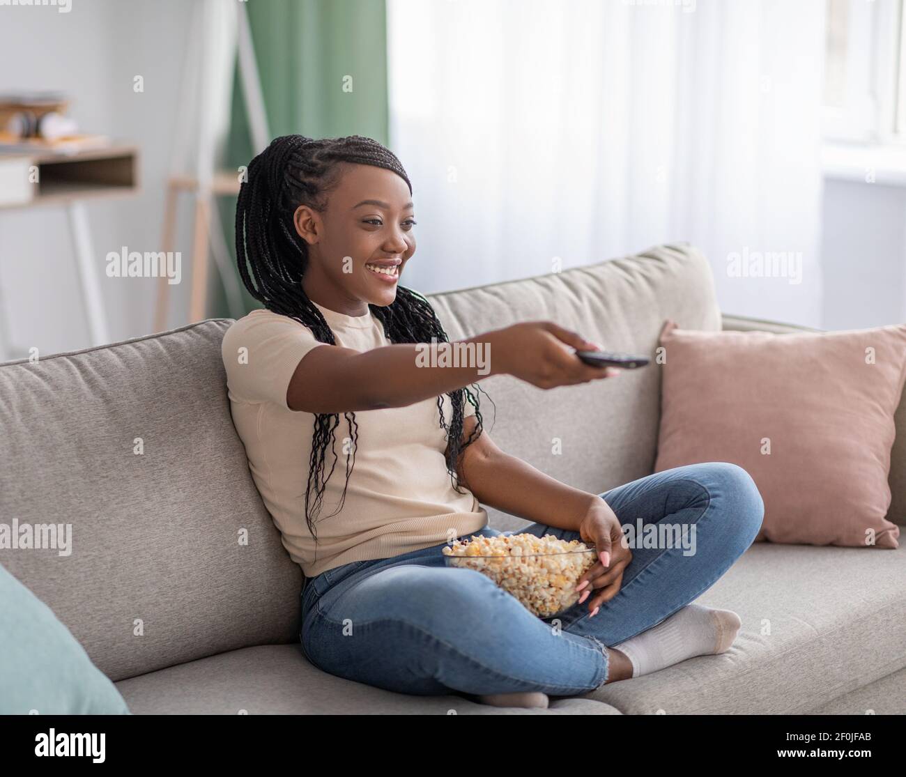 Happy young black woman sitting on couch with TV remote Stock Photo
