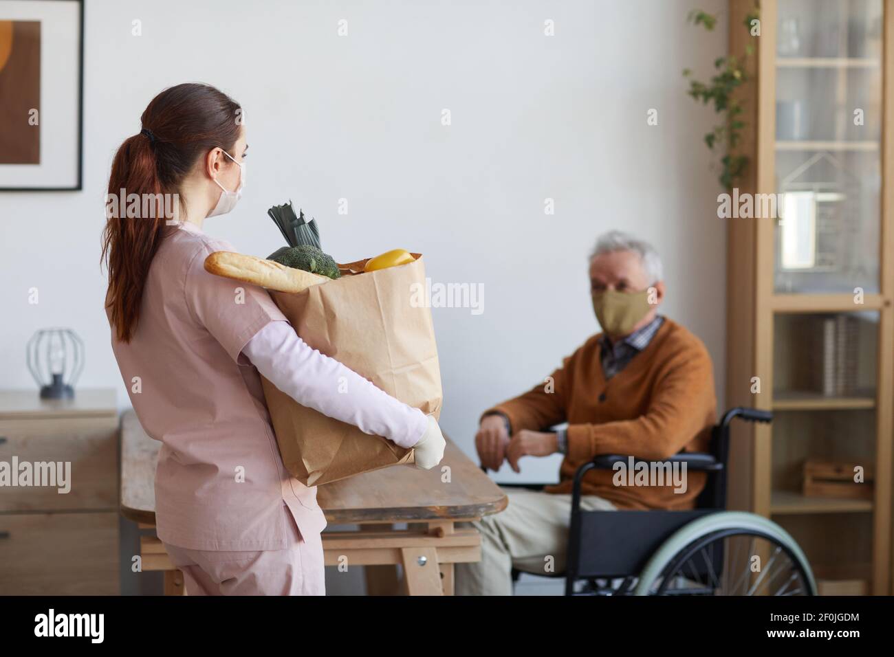 Portrait of female caregiver holding bag with groceries while ...