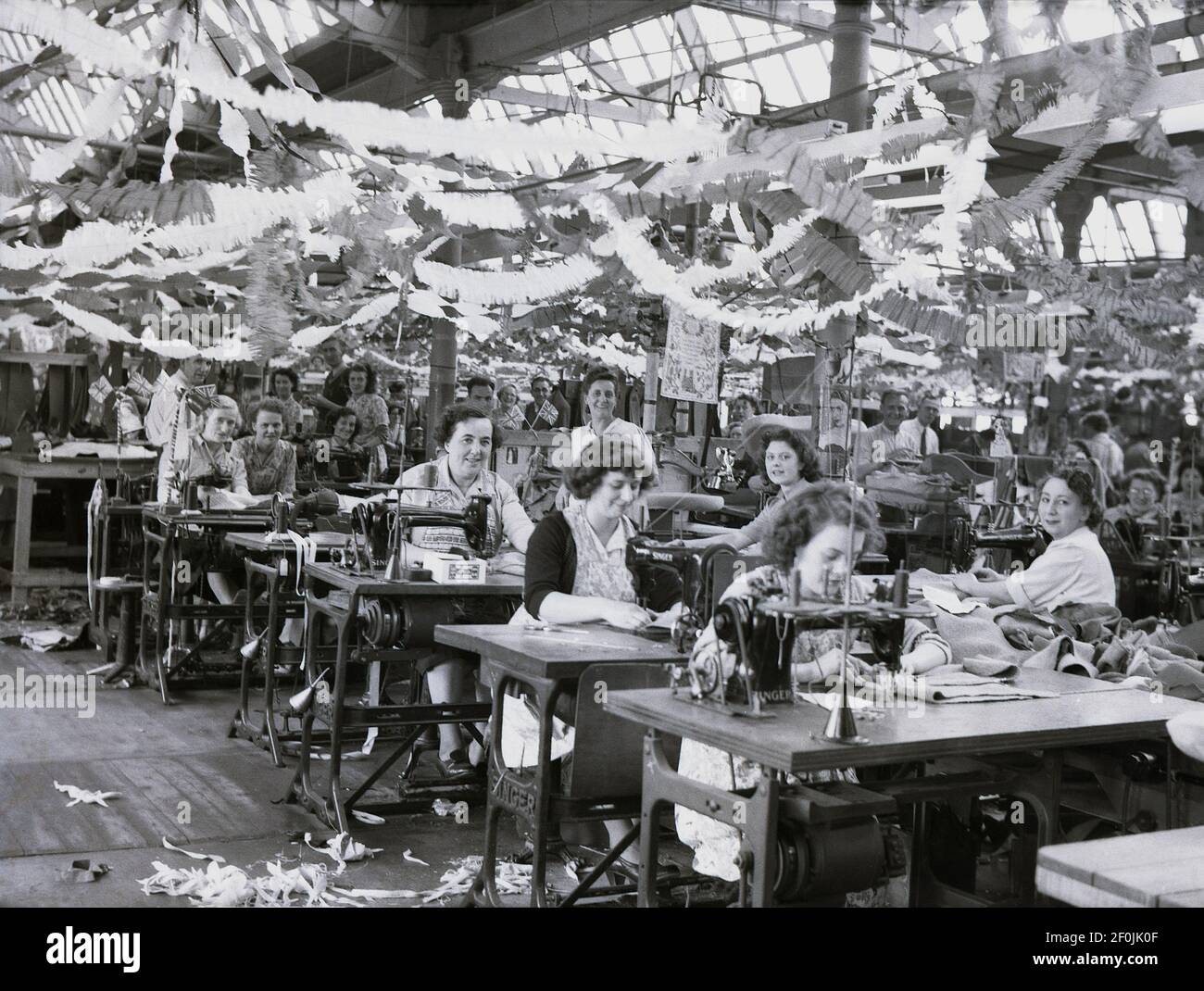 1953, historical, female wiorkers at drapery company, Hepworths of Leeds, England, UK, sitting at work benches witn sowing machines. The factory floor is decorated with bunting and flags celebrating the Queen's coronation. The Providence Works on Clay Pit Lane  was the factory of Joseph Hepworth and Son, a clothing company began in 1865 and which by 1905 had 143 shops. Later in the century, Hepworths became Next. Stock Photo
