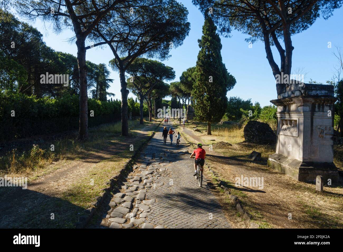 Rome. Italy. People walking and cycling on the Via Appia Antica (Appian Way).  Right, ancient Roman Tomb of the Rabiri (Tomba dei Rabiri). Stock Photo
