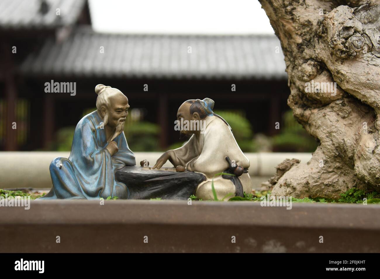 Close up of two small statues of chinese men playing chess near a bonsai inside Chi Lin nunnery in Hong Kong Stock Photo