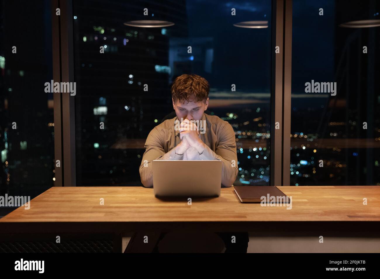 Thoughtful businessman working on laptop at night, developing project strategy Stock Photo