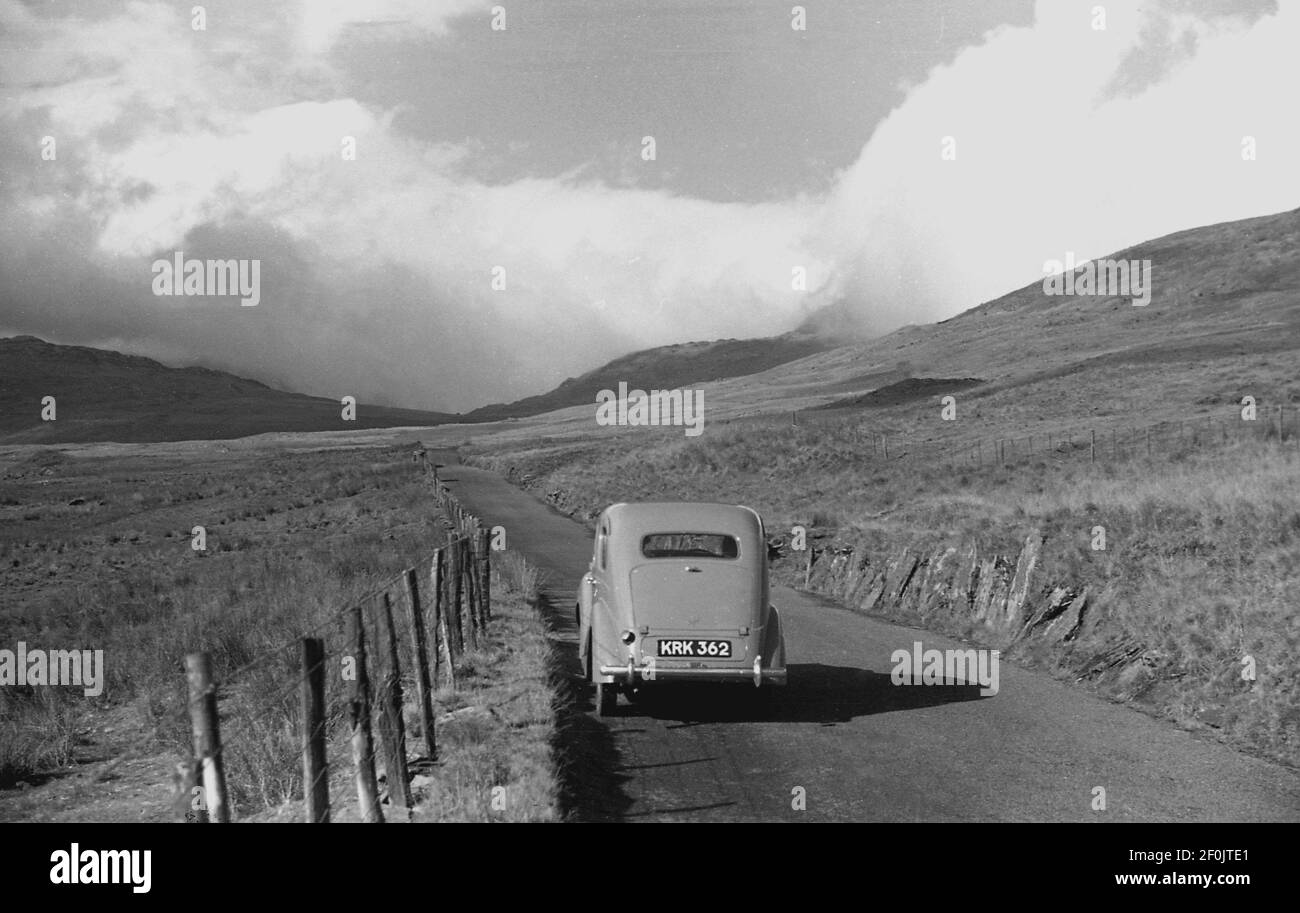 1950s, historical, Touring Wales, a motor car of the era parked on a country lane on the foothills of the Snowdonia mountains, and a blanket of cloud covers the distance landscape. Stock Photo