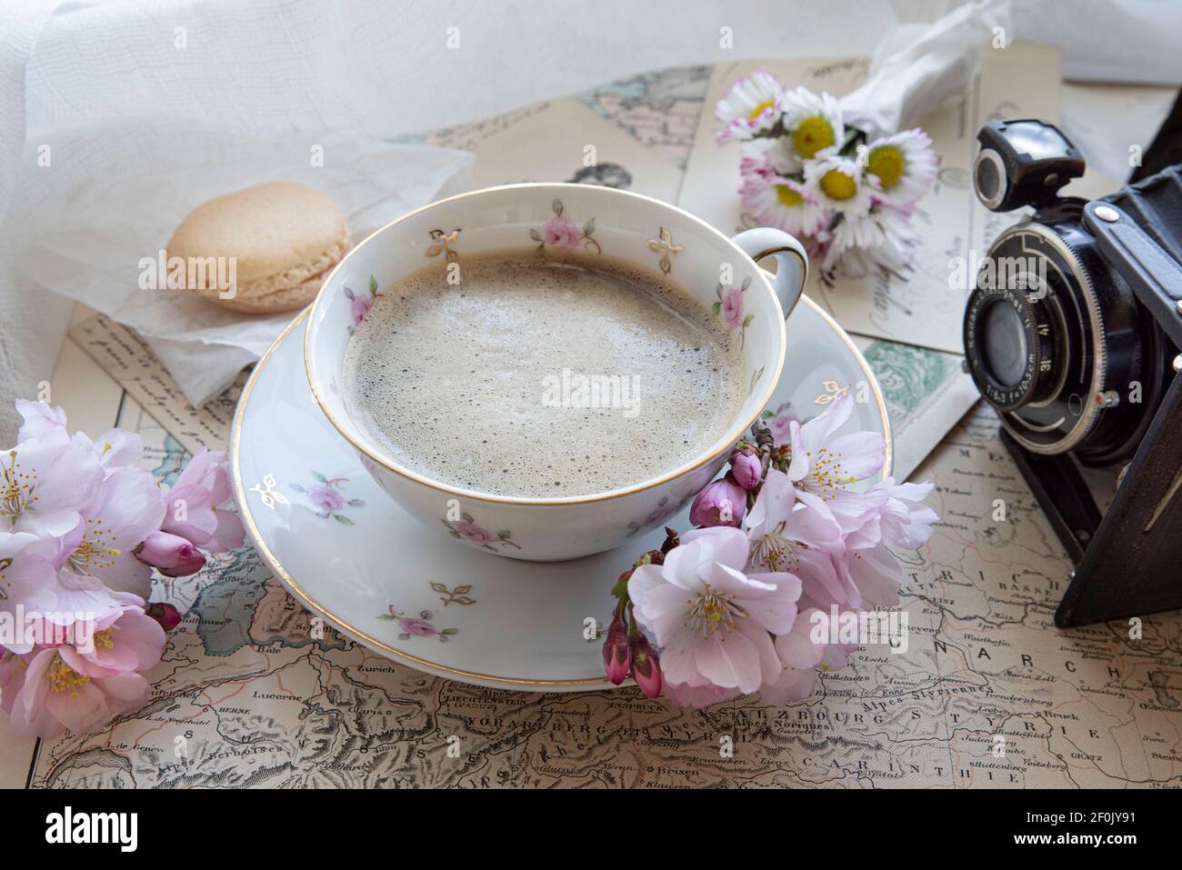 Black coffee in a cup, next to a world map and an old camera with spring flowers on the table Stock Photo