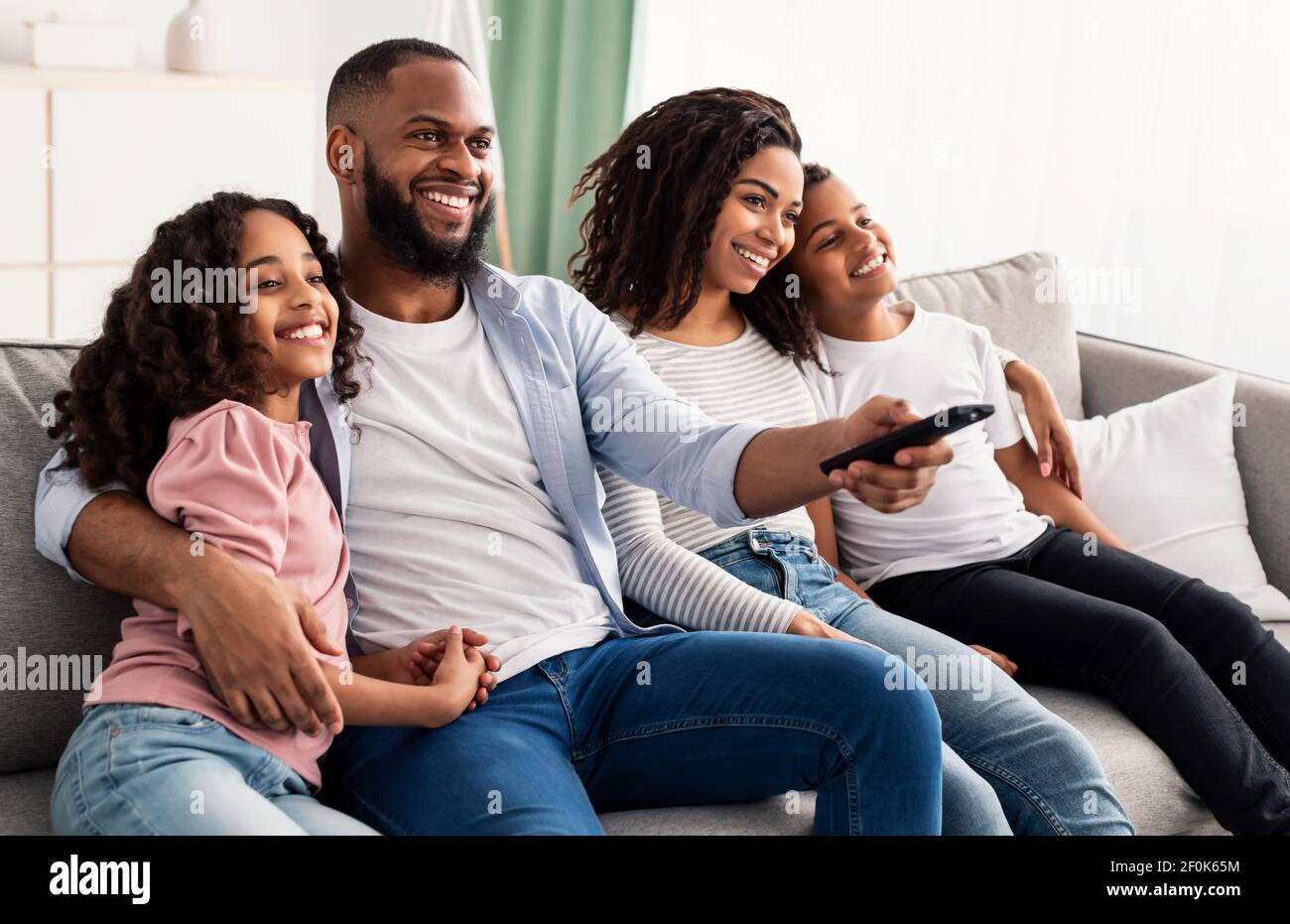 Happy young black family watching television sitting on sofa Stock Photo