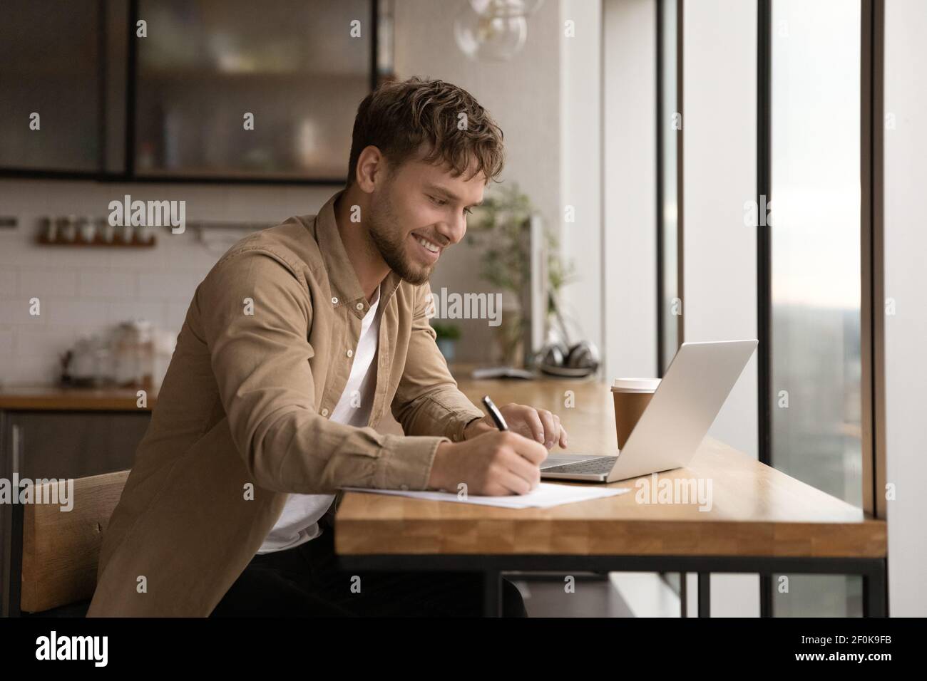 Close up smiling man using laptop, taking notes, studying online Stock Photo