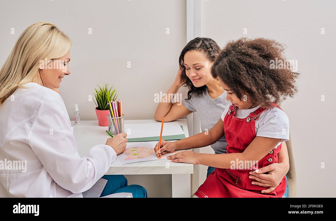 Female psychologist works with African American little girl. Child draws a picture during a psychotherapy session Stock Photo